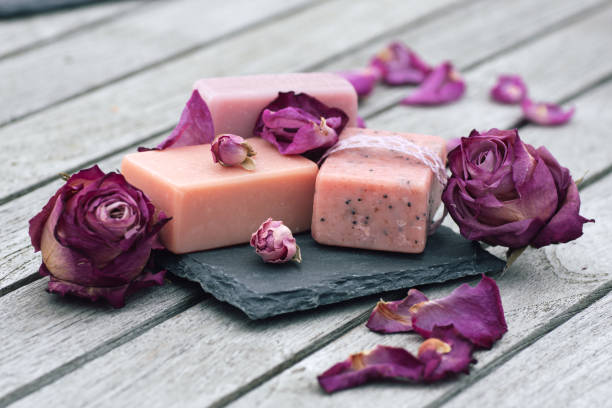 Handmade rose soap bars on dark slate, pink and purple petals on wood